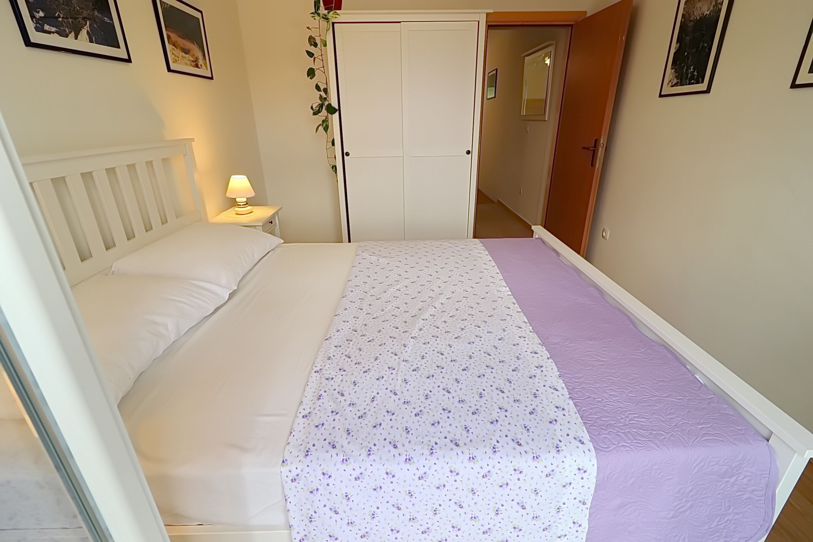 A bedroom with a bed, a nightstand, a wardrobe, and a door leading to another room.