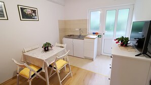 Eine kompakte Küche mit Essbereich, weißen Schränken, einem kleinen Spülbecken und einem Fernseher auf einem Schrank.