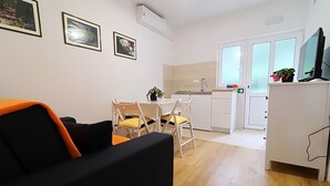 Ein kompakter Wohnbereich mit Sofa, Esstisch, Stühlen, einer Küchenzeile und einem Fernseher.