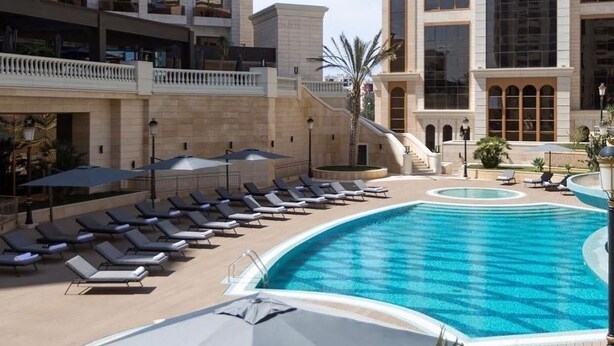 A pool area with lounge chairs and umbrellas, surrounded by buildings with balconies and a clear sky. - Residence Inn by Marriott Algiers Bab Ezzouar (Algiers)