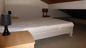Een slaapkamer met een enkel bed, een nachtkastje met een lamp en een stoel.
