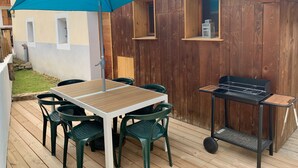 An outdoor patio with a wooden table and chairs, a blue umbrella, and a barbecue grill. - "Tigny House", private chalet in the heart of Valloire, 4 to 6 persons (Valloire)