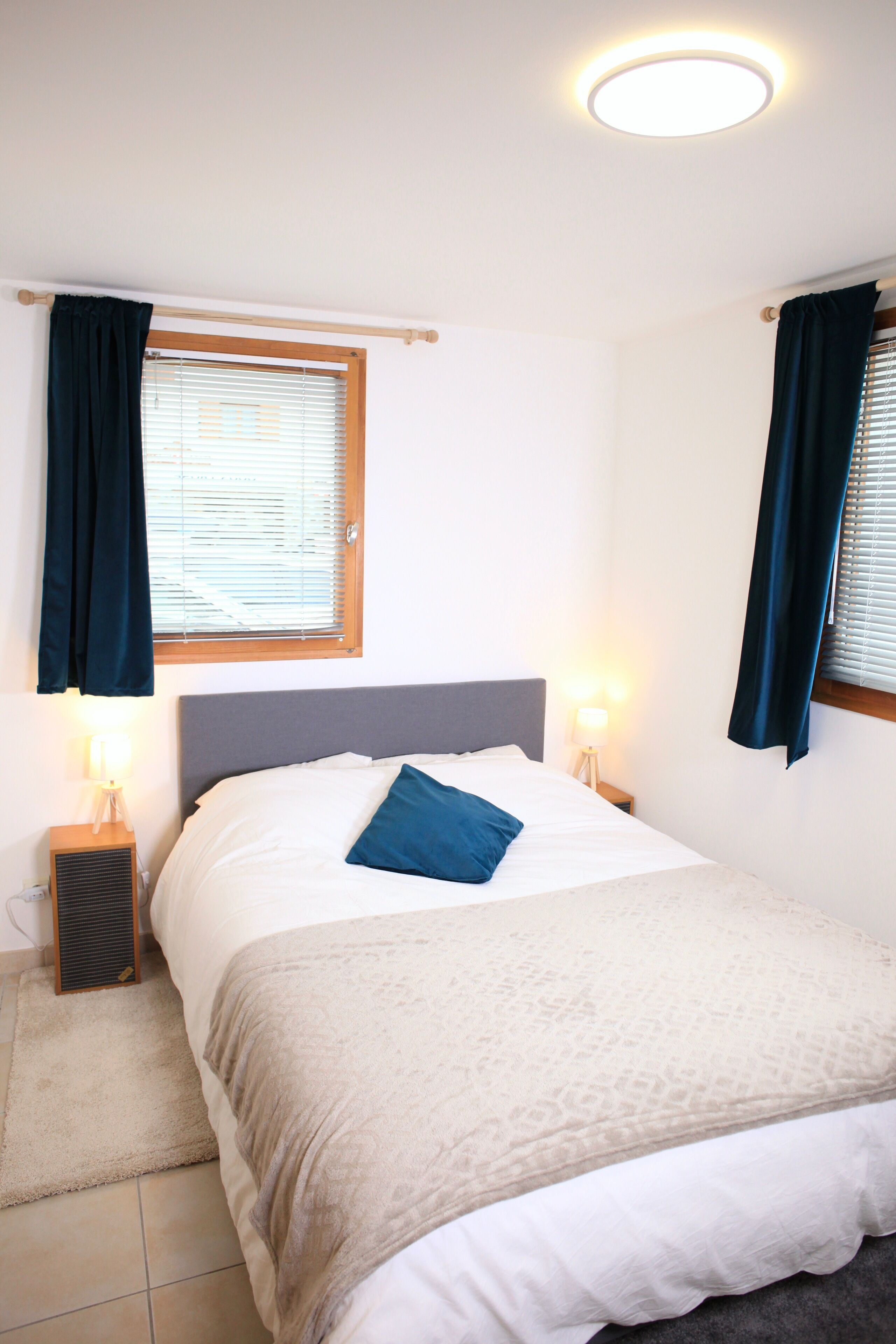 Een slaapkamer met een bed, twee bedlampen, een raam met gordijnen en een plafondlamp.