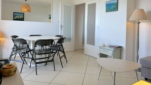 Ein Essbereich mit weißem Tisch und Stühlen, einer hängenden Leuchte, einem kleinen Beistelltisch mit Lampe und einem grauen Sofa.