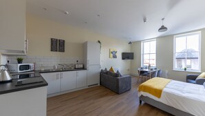 Une cuisine moderne avec des meubles blancs, un canapé gris et un lit recouvert d’une couverture jaune.