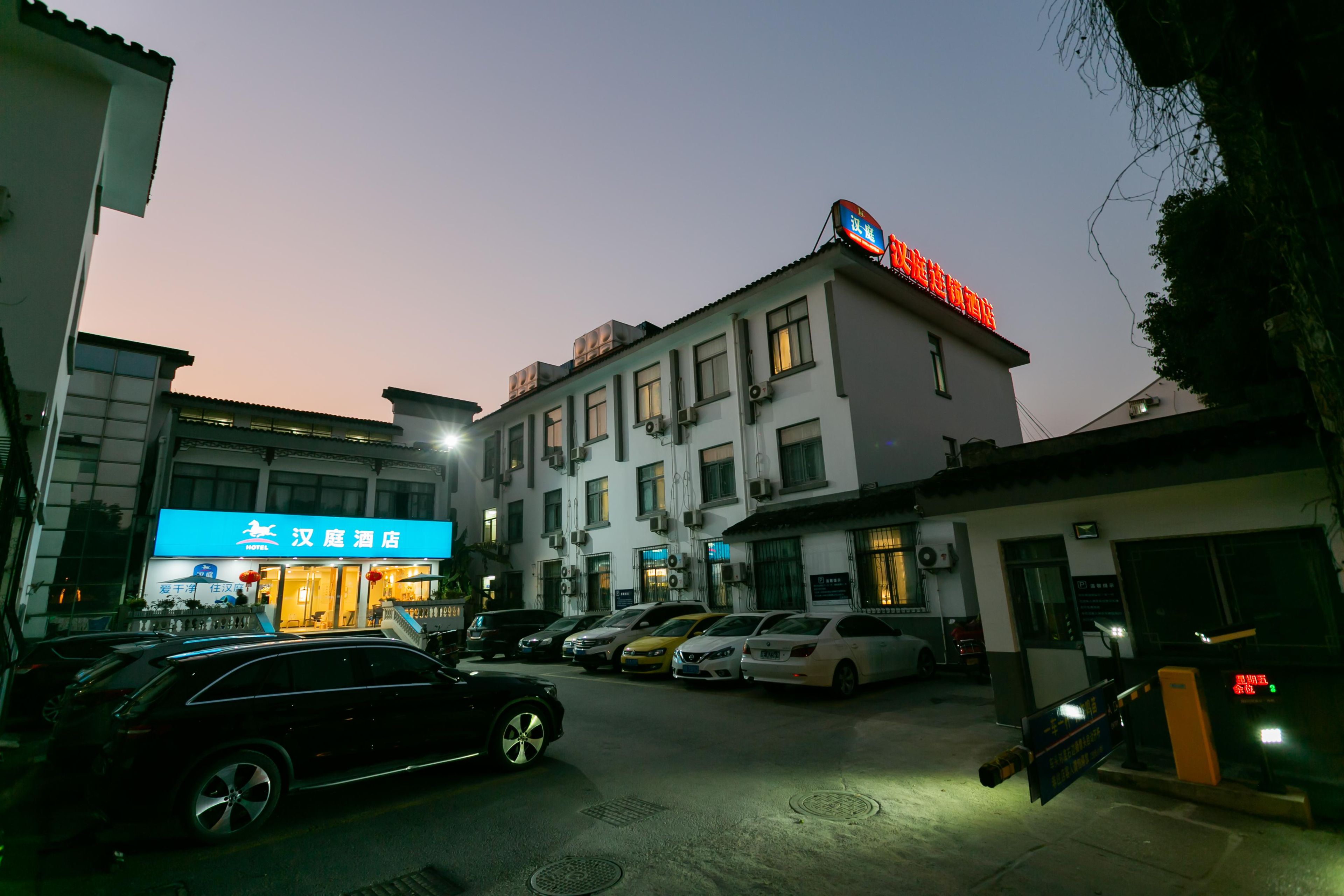Um hotel com vários andares, estacionamento externo e entrada visível.