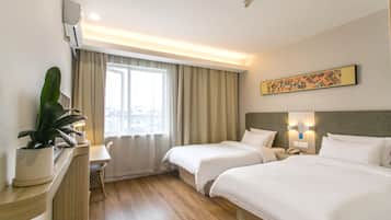 A hotel room with two beds, a desk, a chair, a potted plant, a window with curtains, and a wall-mounted artwork.