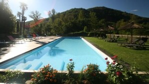 Une piscine rectangulaire à l’eau d’un bleu cristallin, entourée de chaises longues et bordée d’une pelouse, avec une chaîne de montagnes en toile de fond.