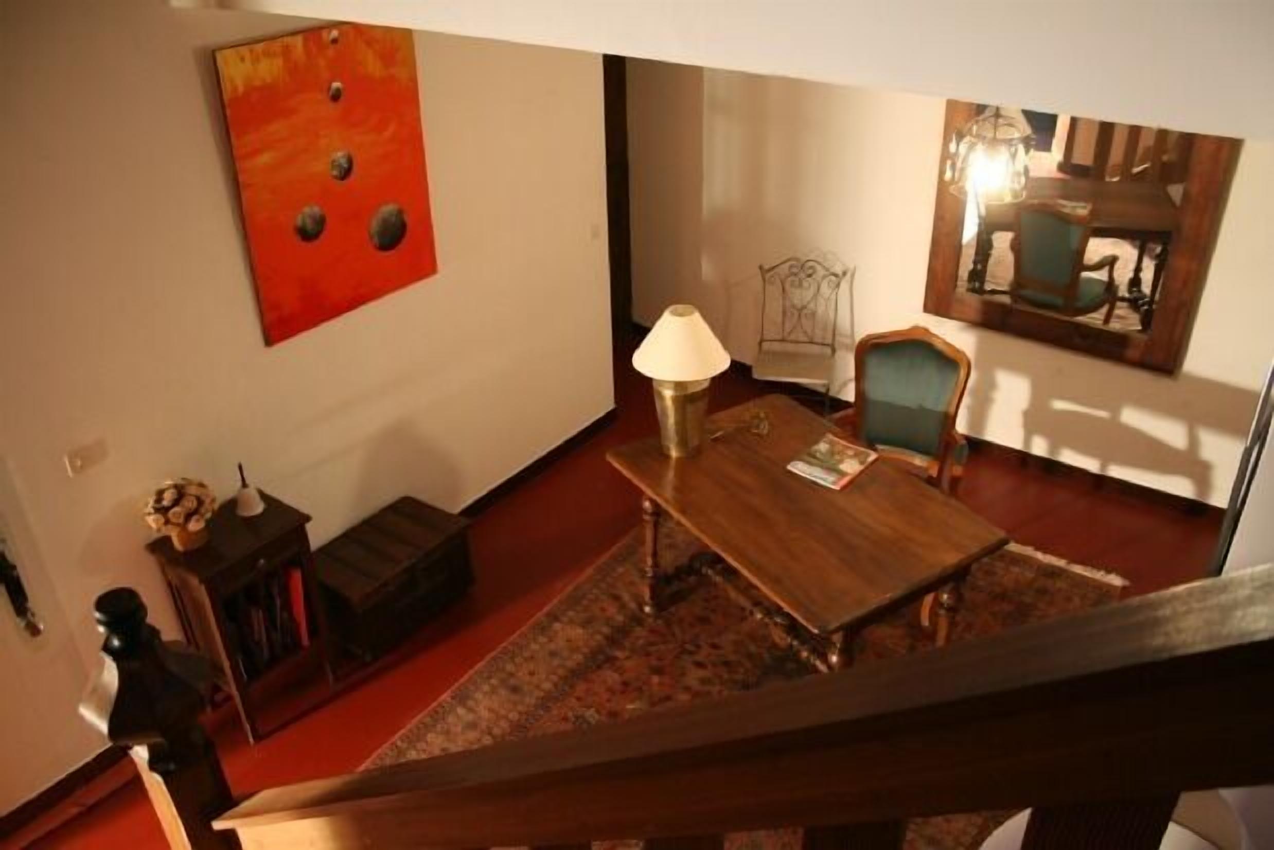 A room with a wooden table, a lamp, a chair, and a red abstract painting on the wall.