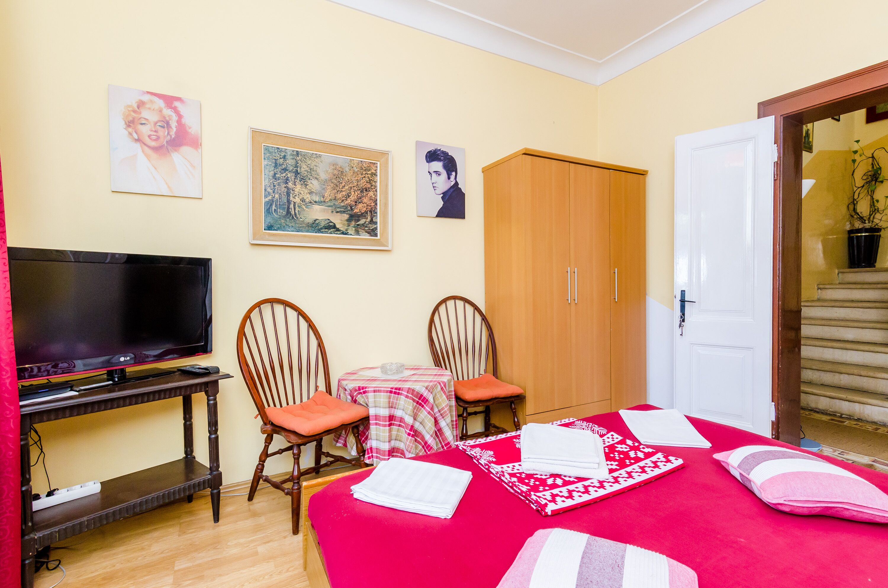 A room with a bed, a TV, two chairs, a table, and a wardrobe.