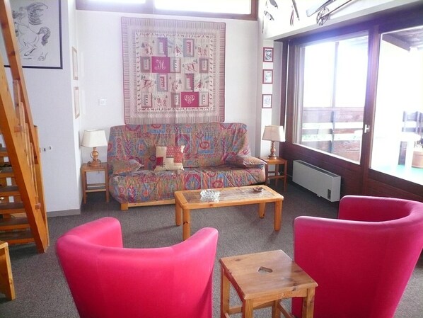 A cozy living room with a colorful sofa, a wooden coffee table, and bright pink chairs. A large window offers a view of the outdoors. - 2-Room Duplex for 7 in Combloux with Parking (Combloux)