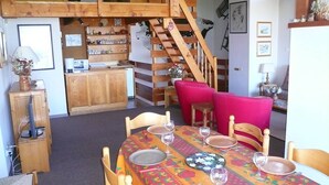 A dining area with a wooden table set for four, surrounded by wooden chairs. A staircase with a wooden railing is visible in the background.