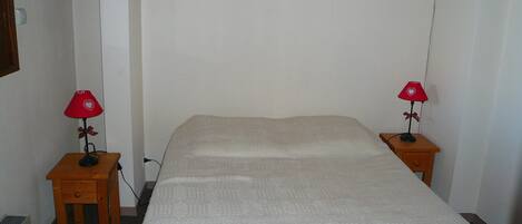 A simple, unadorned room with a single bed, two bedside tables, and two red lamps with heart-shaped lampshades.