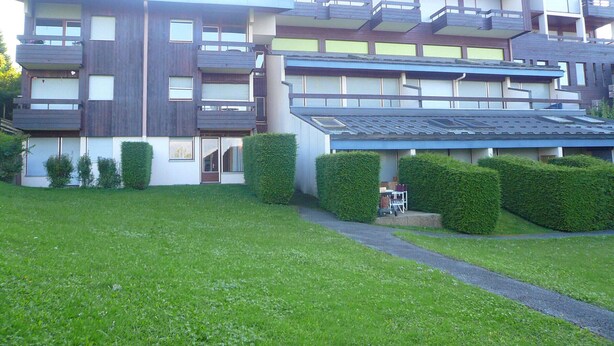A modern multi-story building with balconies, a covered entrance, and a well-maintained lawn.