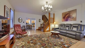 A spacious living room with a large rug, leather furniture, a chandelier, and a staircase leading to another room. - Spacious 4BR Stratton House: A Historic Downtown Stay Backing to Culp's Hill (Gettysburg)