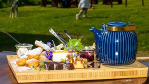 Un montaje para picnic con una tetera azul, pasteles y un tarro de mermelada sobre una tabla de madera.