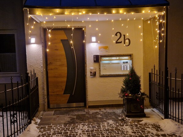L’entrée d’un hôtel, avec une porte en bois, un petit sapin de Noël et une pancarte indiquant le numéro de chambre : « 2b ».