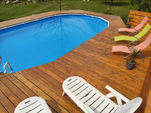 A wooden deck with a swimming pool, lounge chairs, and a table.