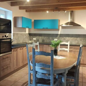 A kitchen with wooden cabinets, a built-in oven, a stove, a dining table with chairs, and a potted plant.