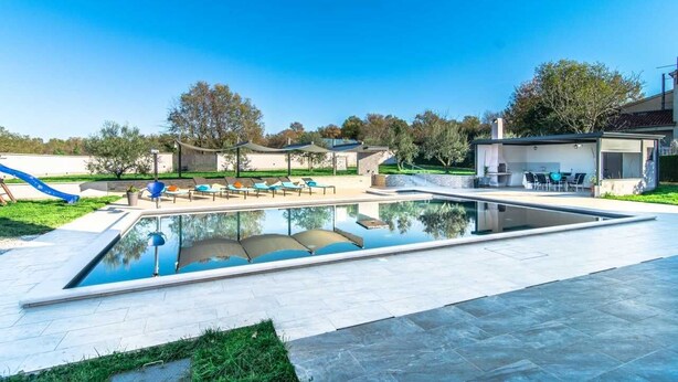 A swimming pool with lounge chairs, a slide, and a patio area with outdoor furniture. - Villa Dolores (Vrsar)