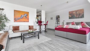 Ein modernes Wohnzimmer mit einem weißen Sofa, einem grauen Sofa, einem roten Sessel, einem Couchtisch und einem roten und weißen Bett.