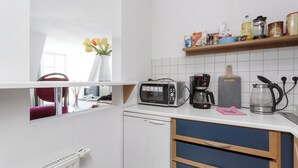 Eine kleine Küche mit Mikrowelle, Toaster, Kaffeemaschine und einem Regal mit verschiedenen Gegenständen.