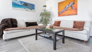 Een moderne woonkamer met een witte bank, een donkerhouten salontafel en een groot schilderij van een strandgezicht.