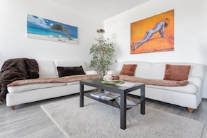 Ein modernes Wohnzimmer mit einem weißen Sofa, einem dunklen Couchtisch und einem großen Gemälde mit Strandmotiv.