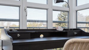 Een kamer met een groot raam, een bureau met een lamp, een stoel en een klein tafeltje met een steen.