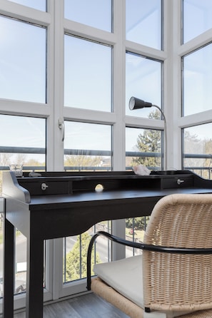 Ein Zimmer mit großem Fenster, Schreibtisch mit Lampe, Stuhl und einem kleinen Tisch mit einem Stein.
