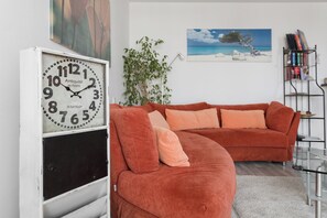 A living room with a large clock, a red sofa, a plant, and a bookshelf. - Saxonia Apartment: a comfortable apartment with a balcony, parking, and an elevator in the building (Dresden)