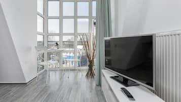 Ein modernes Wohnzimmer mit großem Flachbildfernseher, einem weißen Sofa und einem Esstisch mit Stühlen.