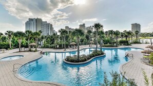 A large outdoor swimming pool surrounded by palm trees and lounge chairs, with high-rise buildings in the background. - Ground floor Studio at Sandestin Luau - close to the beach - (Miaramar Beach)