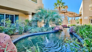 A pool area with a fountain, surrounded by palm trees and rocks, with buildings in the background. - Ground floor Studio at Sandestin Luau - close to the beach - (Miaramar Beach)