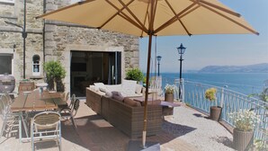 An outdoor patio with a dining table, chairs, a sofa, and an umbrella. - EXCLUSIVE HOUSE PRIVATE BEACH SEA FRONT SLEEPS 13 AMAZING VIEWS (Menai Bridge)