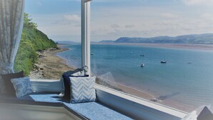 A view from a window seat overlooking a beach with boats, a clear sky, and distant hills. - EXCLUSIVE HOUSE PRIVATE BEACH SEA FRONT SLEEPS 13 AMAZING VIEWS (Menai Bridge)