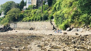 A coastal property with a stone wall, a beach, and a large house with a stone facade and multiple windows. - EXCLUSIVE HOUSE PRIVATE BEACH SEA FRONT SLEEPS 13 AMAZING VIEWS (Menai Bridge)