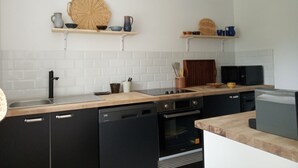 Una cocina moderna con electrodomésticos negros, salpicadero de azulejos blancos, encimeras de madera y estantes con utensilios de cocina.