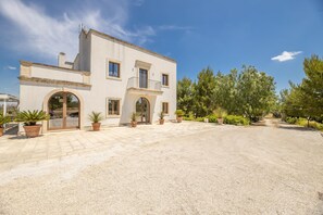 A two-story building with a gravel driveway, potted plants, and a clear blue sky.