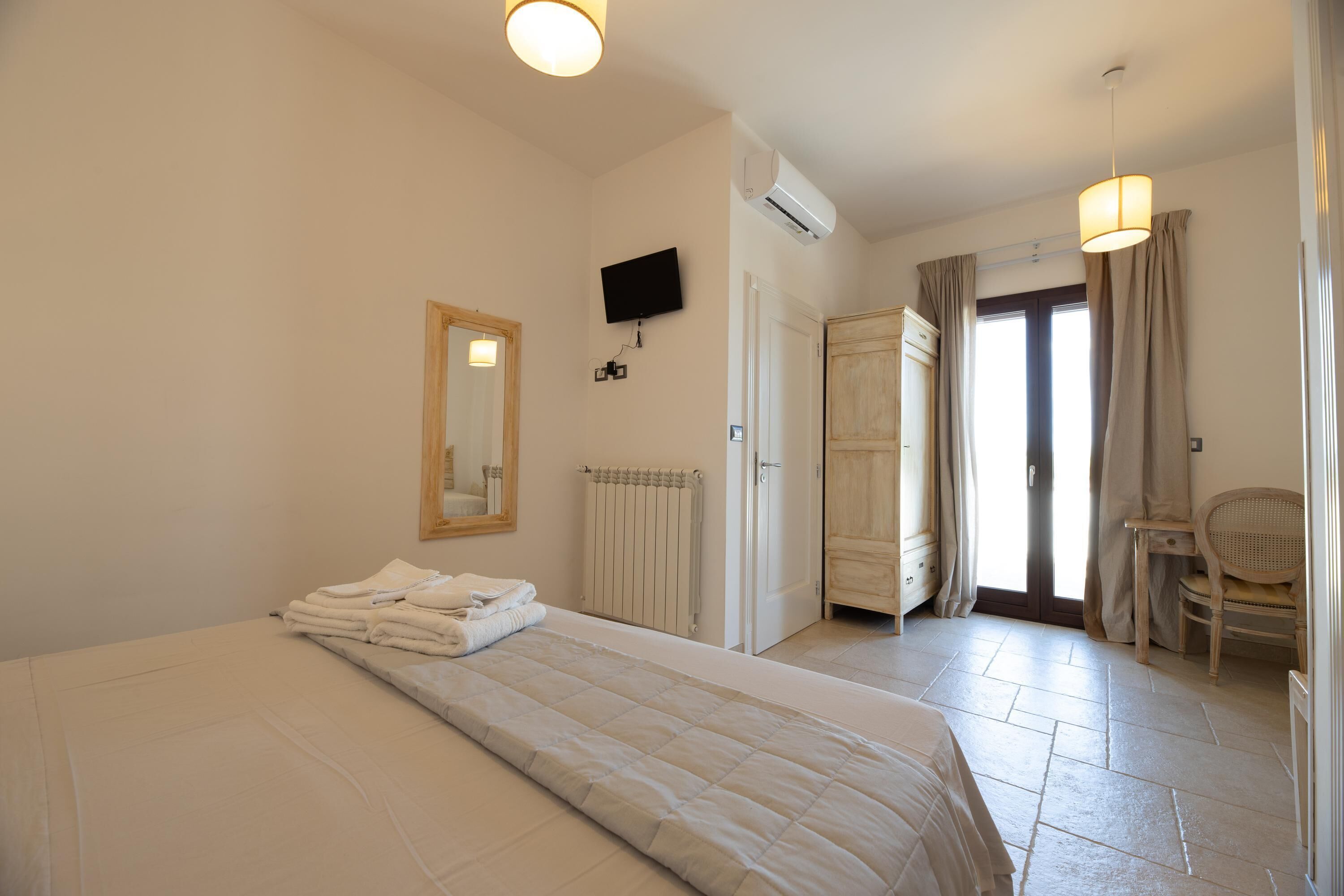 Een hotelkamer met een bed, een televisie, een airconditioningapparaat, een spiegel, een deur en een stoel.