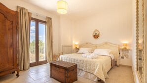 Een slaapkamer met een groot bed, een houten kist, een raam met gordijnen en een spiegel aan de muur.