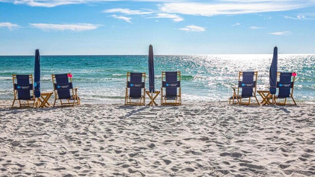 A beach with rows of wooden beach chairs and umbrellas, arranged in a line facing the ocean. - Reba’s Retreat – A Charming Seacrest Beach Escape (Seacrest)