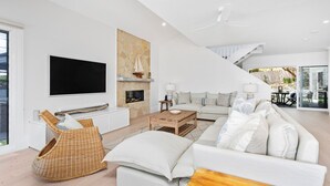 Ein modernes Wohnzimmer mit Flachbildfernseher, Kamin aus Stein, einer Sofagarnitur und einem Essbereich mit Blick ins Freie.