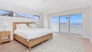 Ein Schlafzimmer mit einem großen Bett, einem Nachttisch, einer Lampe und Meerblick durch eine Schiebetür.