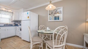 Een keuken met witte kastjes, een koelkast, een eettafel met stoelen en een hanglamp.