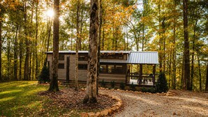 Een chalet met veranda, omgeven door bomen en een grindpad.
