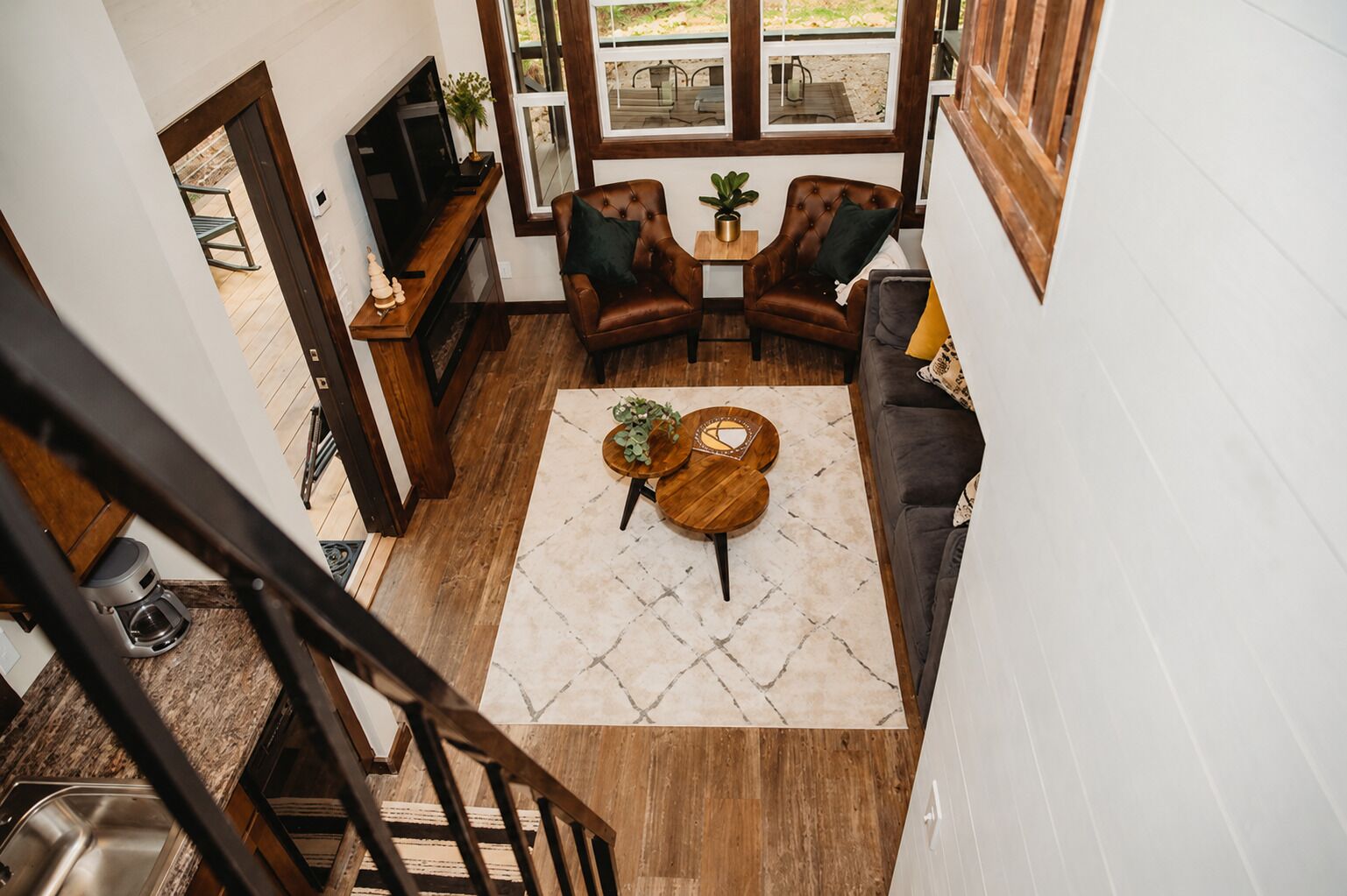 A spacious living area with a dark-colored sofa, two armchairs, a coffee table, and a TV on a wooden stand.