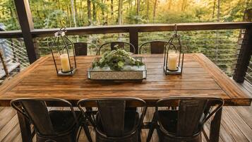 A wooden deck with a table set for four, surrounded by metal chairs, with candles and a plant centerpiece.