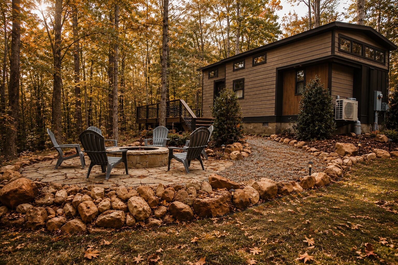 A cabin with a stone fire pit and Adirondack chairs, surrounded by a rock garden and autumn foliage.