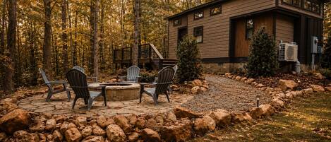 A cabin with a stone fire pit and Adirondack chairs, surrounded by a rock garden and autumn foliage.